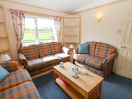 A sitting room with patterned sofas a wooden coffee table with mugs and teapot and windows showing a green field at Row End farm in Brough