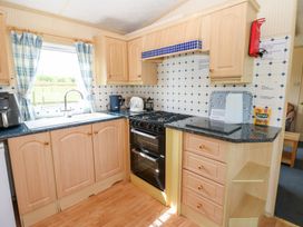 A kitchen with wooden cabinets a gas stove a sink with blue plaid curtains on the window and a countertop with kitchen appliances at Row End farm in Brough