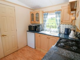 A kitchen with wooden cabinets a gas stove a small refrigerator and a window with blue check curtains at Row End farm in Brough