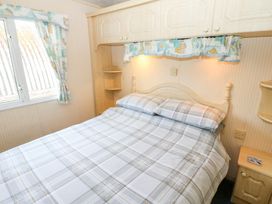 A bedroom with a double bed under built-in wooden cabinets and a window with patterned curtains at Row End farm in Brough