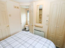A bedroom with a bed covered in a plaid blanket a mirror on the wall a heater built in wooden wardrobes and a door open to a bathroom with a toilet at Row End farm in Brough