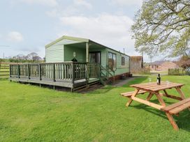 A green mobile home with a wooden deck and picnic table on a lawn at Row End farm in Brough