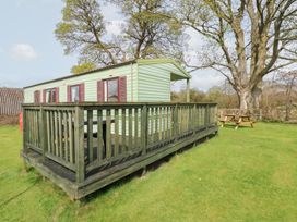 A green caravan with red shutters on a wooden deck on grass near a large tree at Row End farm in Brough