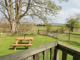 A garden with a wooden picnic table a bottle and glasses on the table green grass trees and a wooden fence at Row End farm in Brough