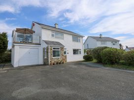 A two-story house with a garage and balcony with outdoor seating and umbrella on a paved driveway at Swn Y Wylan in Bwlchtocyn near Abersoch
