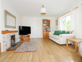 A living room with a sofa with green pillows a wooden bookshelf a television on a wooden stand a fireplace and a rug on a wooden floor at Swn Y Wylan in Bwlchtocyn near Abersoch