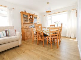 A dining room with a wooden table and chairs a wooden cabinet and a beige sofa with cushions at Swn Y Wylan in Bwlchtocyn near Abersoch