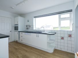 A kitchen with white cabinets black countertops a sink under a large window and wooden floor at Swn Y Wylan Bwlchtocyn near Abersoch