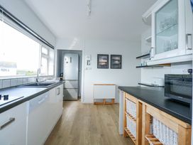 A kitchen with white cabinets a black countertop a refrigerator and wooden storage baskets at Swn Y Wylan in Bwlchtocyn near Abersoch