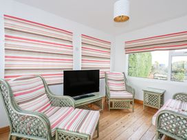 A sitting room with wicker furniture and striped cushions and blinds and a television on a small table at Swn Y Wylan in Bwlchtocyn near Abersoch