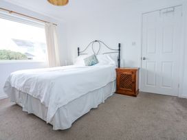 A bedroom with a bed with white bedding a wooden bedside cabinet and a window with curtains at Swn Y Wylan Bwlchtocyn near Abersoch