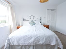 A bedroom with a bed with white bedding and a patterned cushion by a window with curtains at Swn Y Wylan in Bwlchtocyn near Abersoch