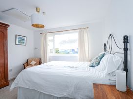 A bedroom with a bed white bedding wooden wardrobe window with curtains and a chair at Swn Y Wylan in Bwlchtocyn near Abersoch