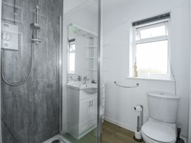 A bathroom with a glass shower enclosure a white sink with cabinet a toilet and a window at Swn Y Wylan Bwlchtocyn near Abersoch