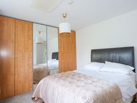A bedroom with a double bed with a black headboard and white bedding and a beige quilt and a wooden wardrobe with mirrored doors at Swn Y Wylan in Bwlchtocyn near Abersoch