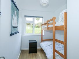 A small bedroom with wooden bunk beds a black bedside table and a window with a view of grass at Swn Y Wylan in Bwlchtocyn near Abersoch
