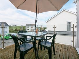 An outdoor balcony with a glass table four black chairs a large umbrella a bottle and glasses on the table at Swn Y Wylan Bwlchtocyn near Abersoch
