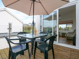 A patio with a glass table and four black chairs under a beige umbrella at Swn Y Wylan in Bwlchtocyn near Abersoch