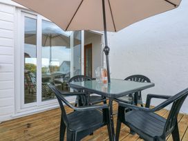 An outdoor patio with a glass table and four black plastic chairs under a beige umbrella at Swn Y Wylan Bwlchtocyn near Abersoch
