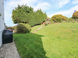 A grassy garden area with a concrete path a black bin shrubs and stairs leading up to a bench at Swn Y Wylan in Bwlchtocyn near Abersoch
