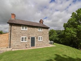A stone house with a grey door and white windows on a grassy lawn with trees in the background at Cae Iocyn in Chirk
