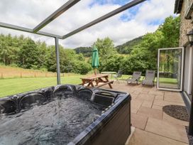 An outdoor patio with a hot tub wooden picnic table green umbrella two lounge chairs and countryside view at Cae Iocyn in Chirk
