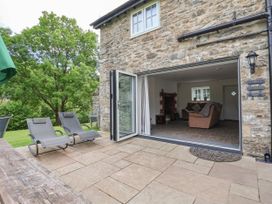 An outdoor patio with two lounge chairs next to a stone house with open folding doors revealing a living room at Cae Iocyn in Chirk