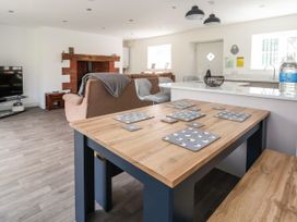 A dining table with placemats and coasters next to a kitchen counter and a living area with sofas and a TV at Cae Iocyn in Chirk