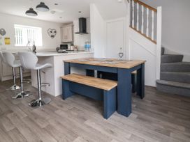 A kitchen and dining area with a wooden table and bench a white counter with three bar stools and stairs in the background at Cae Iocyn in Chirk