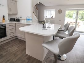 A kitchen with a white countertop island three bar stools and sliding glass doors at Cae Iocyn in Chirk