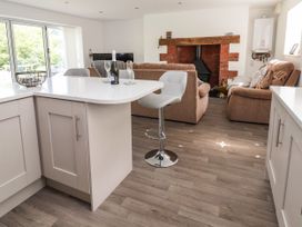 A kitchen island with two glasses and a bottle on it stools in front of a fireplace with brown sofas in a living room at Cae Iocyn in Chirk