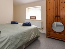 A bedroom with a bed covered with green quilt and folded towels next to a window and a wooden wardrobe with a circular mirror at Cae Iocyn in Chirk