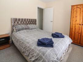 A bedroom with a double bed with gray bedding and two folded blue towels on it a wooden wardrobe a wooden bedside table and a white door at Cae Iocyn in Chirk