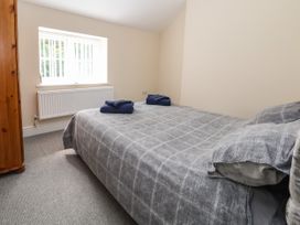 A bedroom with a double bed covered with a gray checked duvet and two folded towels on top near a window with vertical blinds at Cae Iocyn in Chirk