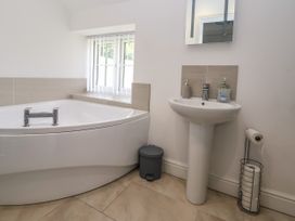A bathroom with a corner bathtub a pedestal sink a small window and a toilet paper holder at Cae Iocyn in Chirk