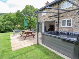 A patio area with picnic table umbrella lounge chairs and a hot tub next to a stone house at Cae Iocyn in Chirk