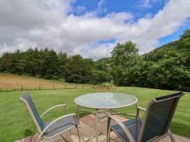 A glass top table with two chairs on a lawn surrounded by trees at Cae Iocyn in Chirk