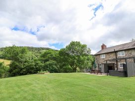 A stone house with a patio area and outdoor furniture on a large lawn surrounded by trees at Cae Iocyn in Chirk