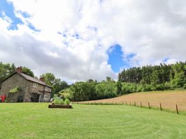 A stone house with chimney on a lawn next to a garden bed and trees at Cae Iocyn in Chirk