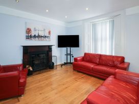 A living room with red leather sofas a television on a stand a fireplace with a painting above it and vertical blinds on the window at 11 Magdalene Road in Torquay