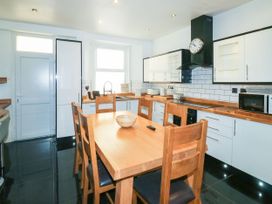 A kitchen with a wooden dining table and chairs a white door a window white cabinets and a microwave at 11 Magdalene Road Torquay