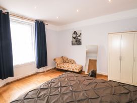 A bedroom with a bed covered in a gray blanket a chaise lounge with floral upholstery a standing mirror a wardrobe and dark curtains on a window at 11 Magdalene Road in Torquay