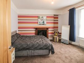 A bedroom with a double bed, striped wallpaper, a wooden fireplace, a chair, a full-length mirror, and blue curtains at 11 Magdalene Road in Torquay