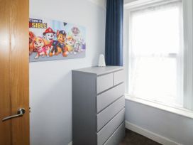 A small room with a grey chest of drawers under a window with white curtains and a Paw Patrol poster on the wall at 11 Magdalene Road in Torquay