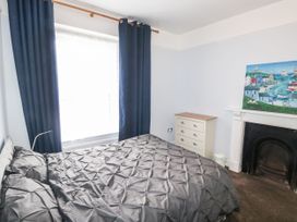A bedroom with a bed covered in a gray quilt next to a window with dark blue curtains and a white chest of drawers beside a fireplace with a painting above at 11 Magdalene Road in Torquay