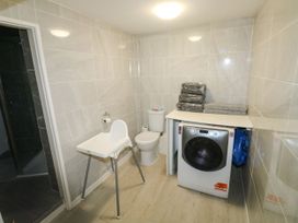A tiled utility room with a toilet, high chair, washing machine, and folded towels on top at 11 Magdalene Road in Torquay