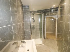 A bathroom with gray tiled walls and floor a white sink and a glass shower enclosure at 11 Magdalene Road in Torquay