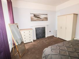 A bedroom with a standing mirror next to a chest of drawers a closed wardrobe a bed with a gray bedspread and a painting above a covered fireplace at 11 Magdalene Road in Torquay