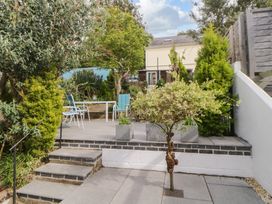 A garden patio with steps leading to a seating area with chairs and table surrounded by trees and plants at Midhurst in Brixham