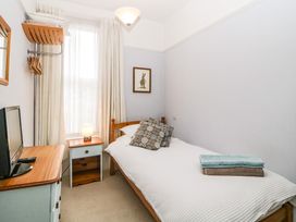 A small bedroom with a single bed with pillows and folded towels a nightstand with a lamp a dresser with a television and a wall-mounted clothes rack at Midhurst in Brixham